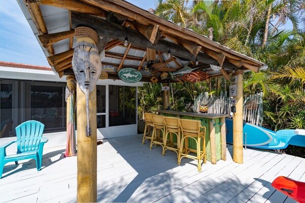 Una terraza de madera con un bar tiki, taburetes de bar y una silla azul.