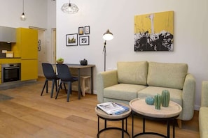 A living room with a sofa, a dining table with chairs, a lamp, and a painting on the wall.