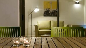 Una mesa de madera con tres velas encendidas, una silla verde, un sofá y una lámpara de pie en una habitación con un cuadro en la pared.