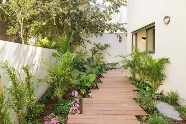 A wooden pathway leading through a garden with various plants and flowers.