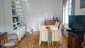 Un comedor con una mesa dispuesta para cuatro personas, un televisor sobre un mueble, una estantería y una escalera.