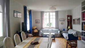 Una sala de estar con una mesa de comedor, sillas, un sofá, un televisor y una estantería.