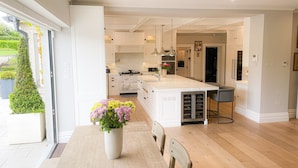 A modern kitchen with white cabinetry, a large island, and a dining area with a table and chairs. - Cluain Ard Holiday Home (Castletown)
