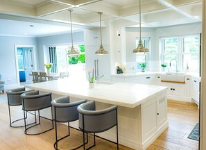 A spacious kitchen with a large island, bar stools, pendant lights, and a view of the outdoors. - Cluain Ard Holiday Home (Castletown)