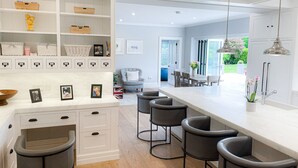 A modern kitchen with a white countertop, bar stools, and a view into the dining area. - Cluain Ard Holiday Home (Castletown)