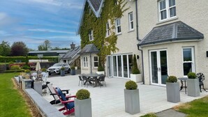 A spacious patio with a dining area, outdoor seating, and a car parked nearby. - Cluain Ard Holiday Home (Castletown)