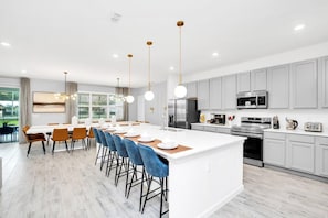 A modern kitchen with a central island, white cabinetry, and stainless steel appliances. - Themed Rooms | Mario Kart | Private Pool | Disney (Kissimmee)