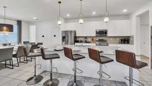 Uma cozinha moderna com armários brancos, eletrodomésticos de aço inoxidável e uma ilha central com banquetas.