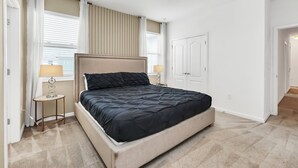 Quarto com uma cama, duas mesas de cabeceira, uma janela com persianas, uma porta e chão coberto de carpete.