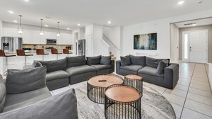 Uma sala de estar moderna com sofás cinzas, uma mesa de centro e uma cozinha ao fundo.