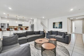 A modern living room with grey sofas, a coffee table, and a kitchen in the background.