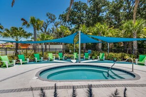 Una piscina de forma circular, envoltada de gandules verdes i una zona amb toldes blaves.