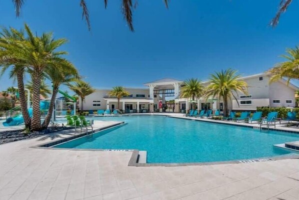 A swimming pool with lounge chairs, palm trees, and a building with multiple windows.