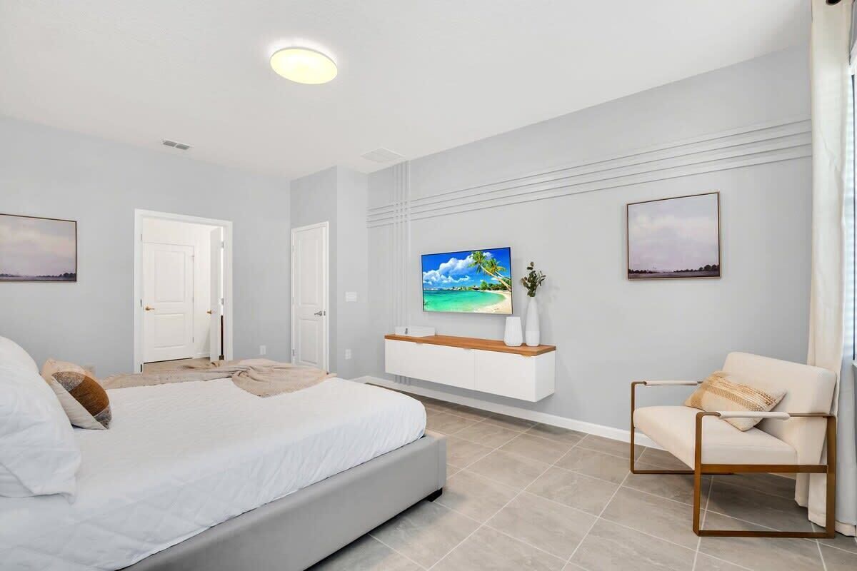 Ein modernes Schlafzimmer mit einem großen Bett, einem an der Wand montierten Fernseher und einer Sitzecke mit einem Sessel.