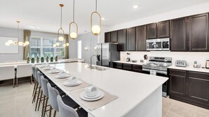 A modern kitchen with a central island, dark cabinetry, stainless steel appliances, and pendant lighting.