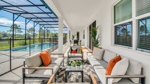 A covered outdoor seating area with a pool, white walls, and large windows.