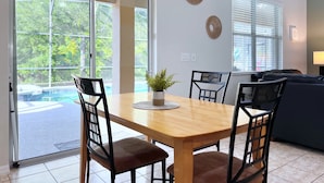 A dining area with a wooden table, four chairs, a potted plant, and a view of a swimming pool through glass doors.