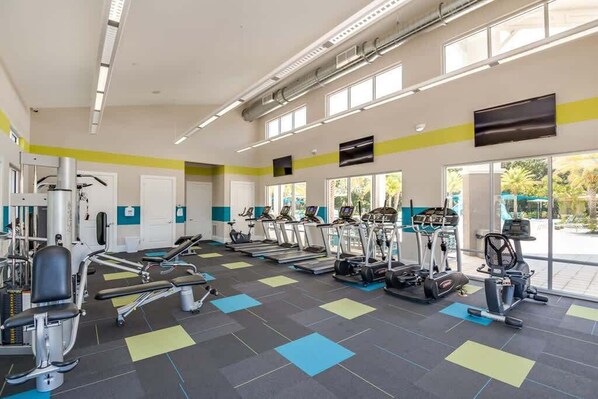 Une salle de sport équipée de tapis de course, de vélos elliptiques et de postes d'entraînement avec poids.