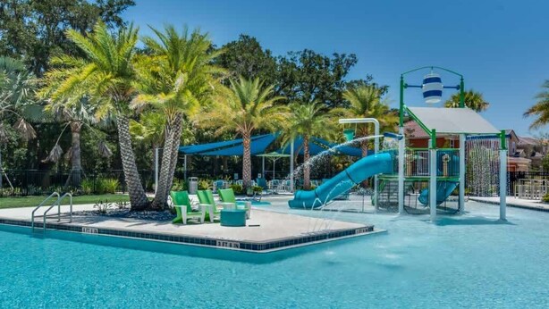 A swimming pool with a water slide, lounge chairs, and palm trees.