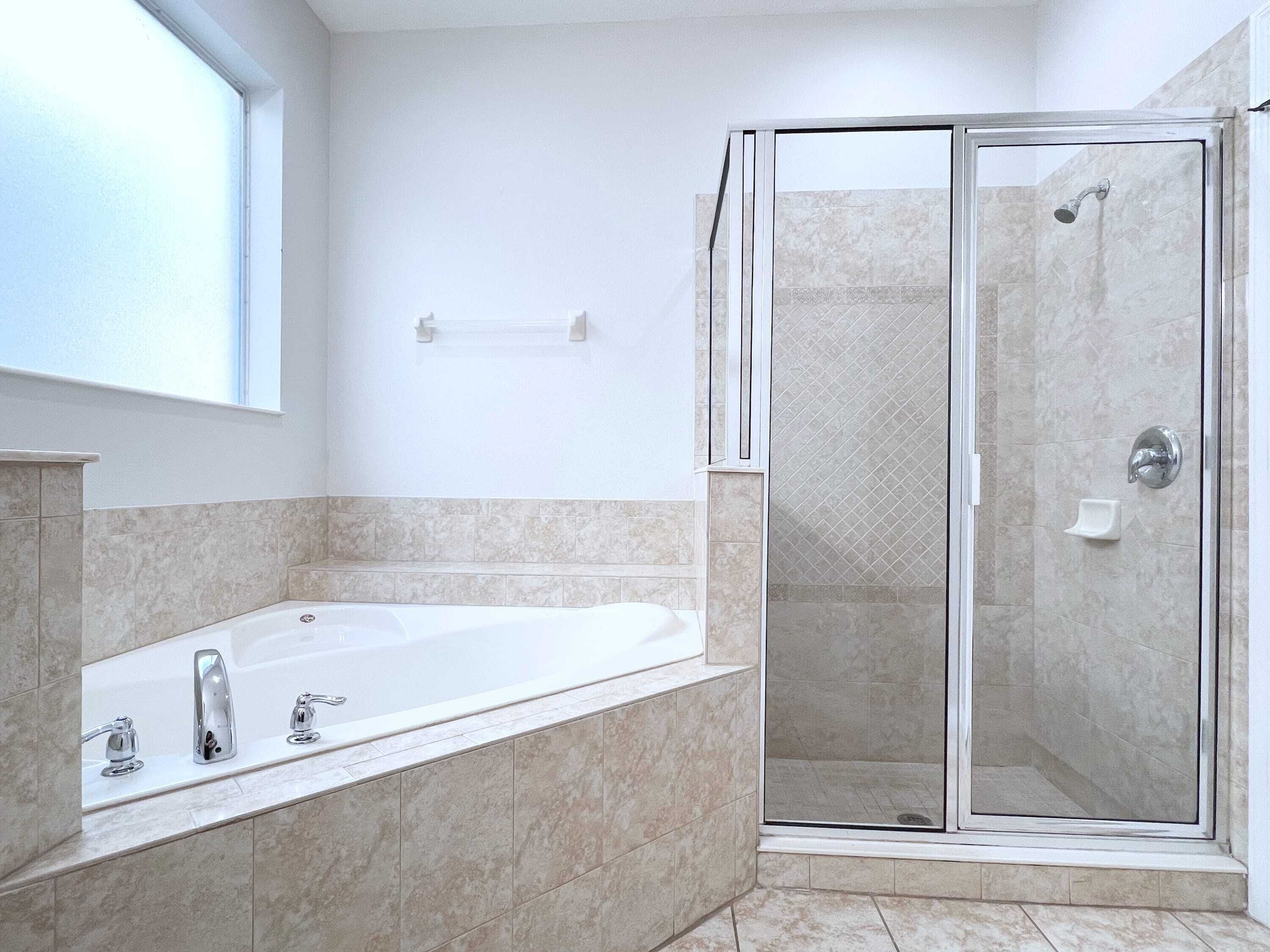 Een moderne badkamer met een douche met glazen wand, een vrijstaand bad en een raam voor natuurlijk licht.