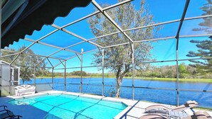 Area piscina con vista su un lago, circondata da una recinzione metallica e alberi.
