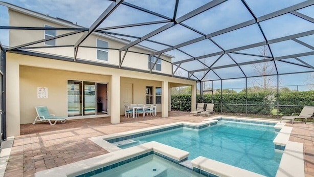 A swimming pool with a glass-enclosed patio area, outdoor seating, and a covered section with a table and chairs.