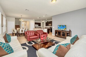 A modern living room with a white sofa, red leather chairs, a glass coffee table, and a kitchen in the background.
