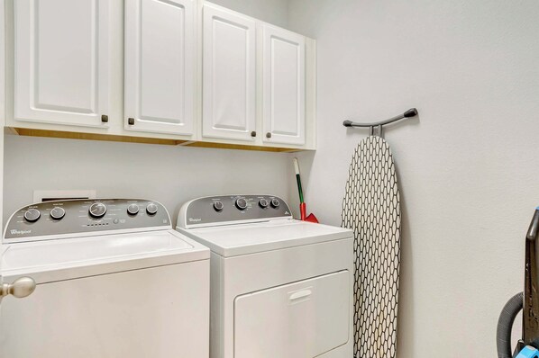 A laundry area with a front-loading washer and dryer, white cabinets above, and a hanging rack with a patterned item.