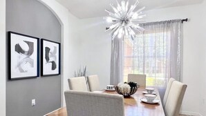 A dining area with a wooden table, six chairs, a chandelier, and two framed artworks on the wall.