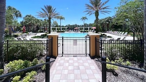 A pool area with a tiled walkway leading to the pool, surrounded by palm trees and lounge chairs.