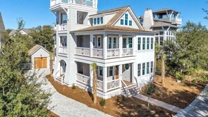 A large, multi-story house with a prominent balcony on the upper floor, a covered front porch, and a garage.