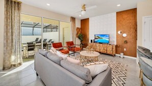 A modern living room with a sofa, chairs, a TV, and a dining area with a glass wall. - Value! Clean! Lazy River-Resort 6 mi 2 Disney! 108 (Davenport)