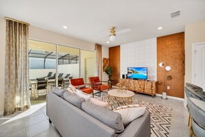 Een moderne woonkamer met een bank, stoelen, een televisie en een eetgedeelte met glazen wand.