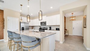 A modern kitchen with a central island, bar stools, stainless steel appliances, and pendant lighting. - Value! Clean! Lazy River-Resort 6 mi 2 Disney! 108 (Davenport)