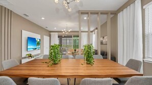 A modern conference room with a wooden table, grey chairs, and a large chandelier. - Frozen | Hero Gameroom | Pool | Near Disney 1806 (Davenport)