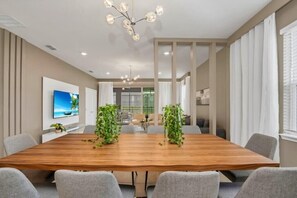 A modern conference room with a wooden table, grey chairs, and a large chandelier. - Frozen | Hero Gameroom | Pool | Near Disney 1806 (Davenport)