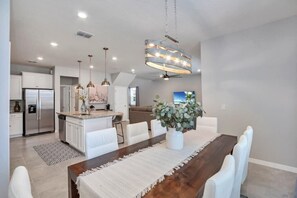 A modern kitchen with white cabinetry, a stainless steel refrigerator, and pendant lighting.
