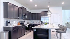 A modern kitchen with dark cabinets, stainless steel appliances, and a central island with bar stools. - Star Wars | Themed Rooms | Resort Near Disney 2061 (Davenport)