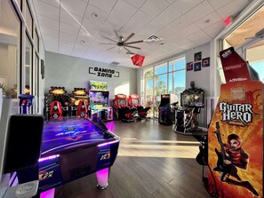 A gaming zone with various arcade machines, a pool table, and a ceiling fan.