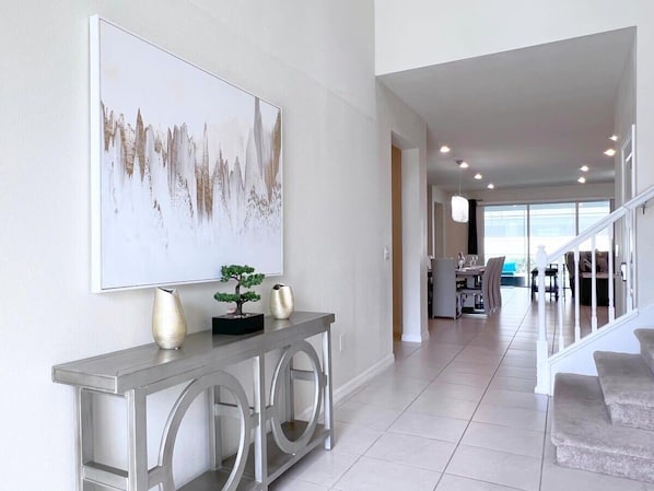 A modern interior with a console table, a large abstract painting, and a staircase leading to a dining area.