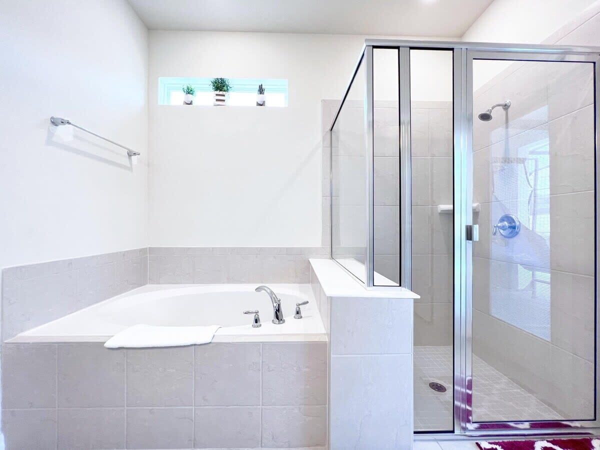 Un baño moderno con una bañera independiente, ducha con mampara de vidrio y un pequeño estante con plantas en macetas.