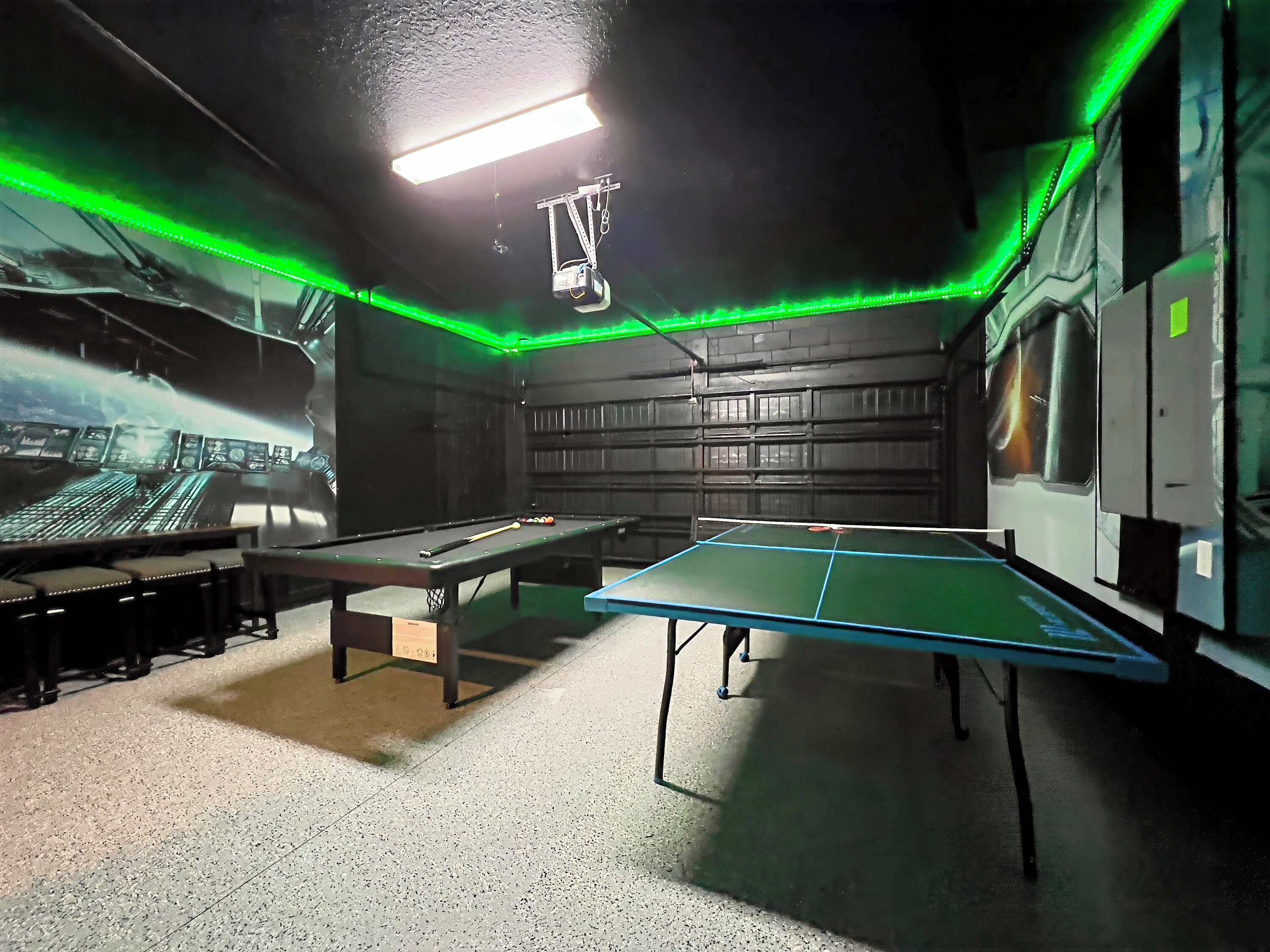 Una sala de billar con mesa de billar, mesa de snooker y una pantalla de proyección mostrando un paisaje urbano.