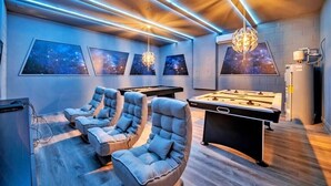 A room with a pool table, two lounge chairs, and a foosball table.