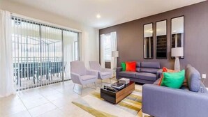 Een moderne woonkamer met een grijze bank, twee fauteuils, een salontafel en een groot raam met jaloezieën.