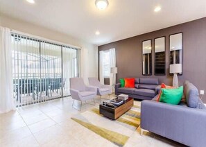 Relax in this spacious living room with a sofa set, armchairs, and a coffee table, offering a view of the outdoors from the balcony.