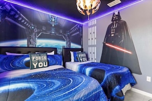 A bedroom with two beds, Star Wars-themed decor, including a Darth Vader poster and a galaxy-themed bedspread.