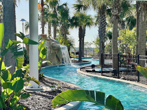 A pool area with a waterfall feature, surrounded by palm trees and tropical plants.