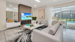 A modern living room with a flat-screen TV, a white sofa, a coffee table, and a large window overlooking a pool.