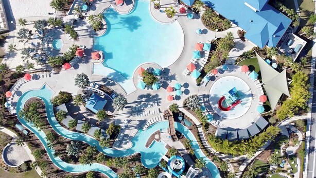 An aerial view of a resort with a large central pool, multiple water slides, and sun loungers.