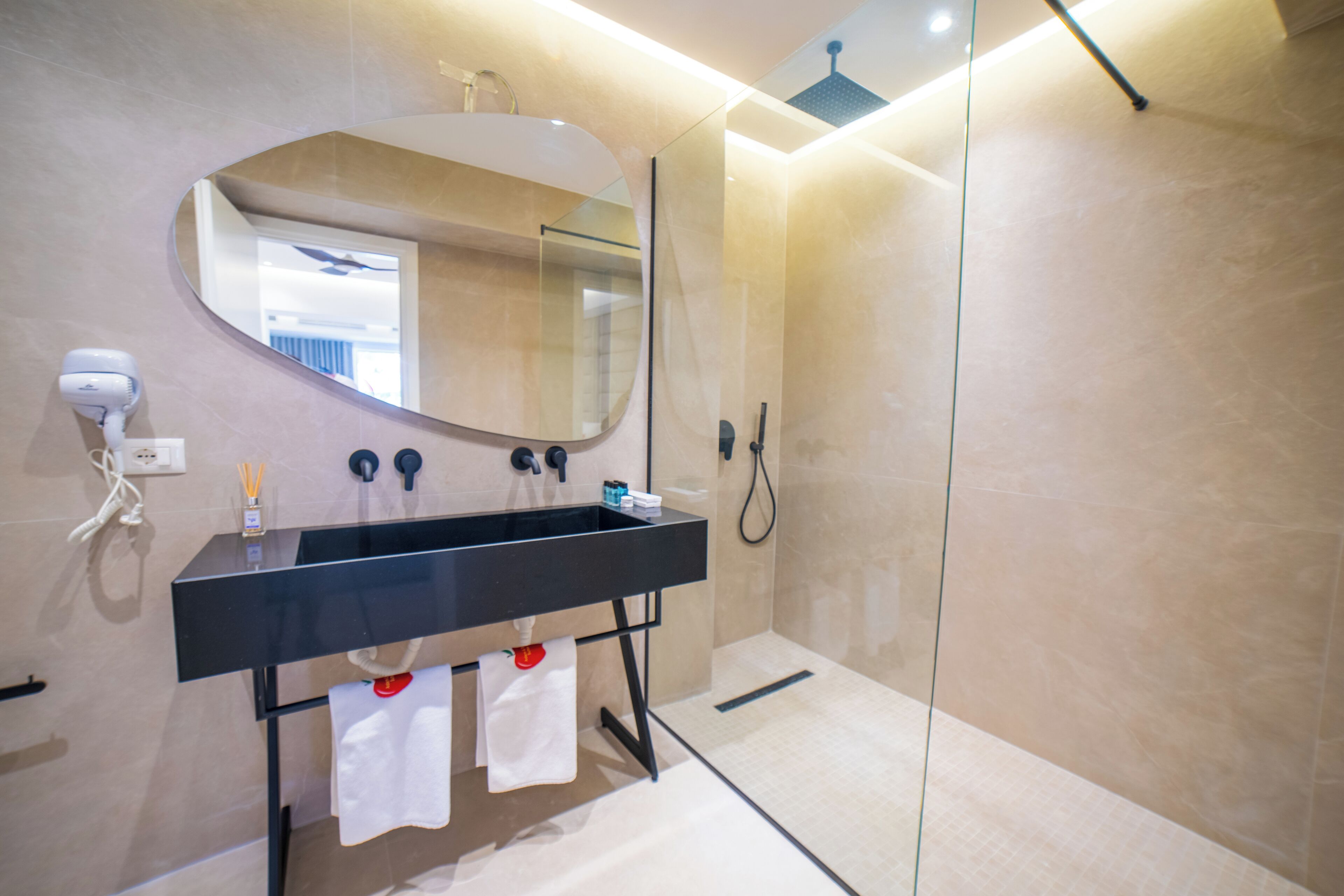 Un baño moderno con un lavamanos negro, un espejo grande y una ducha con cerramiento de vidrio.